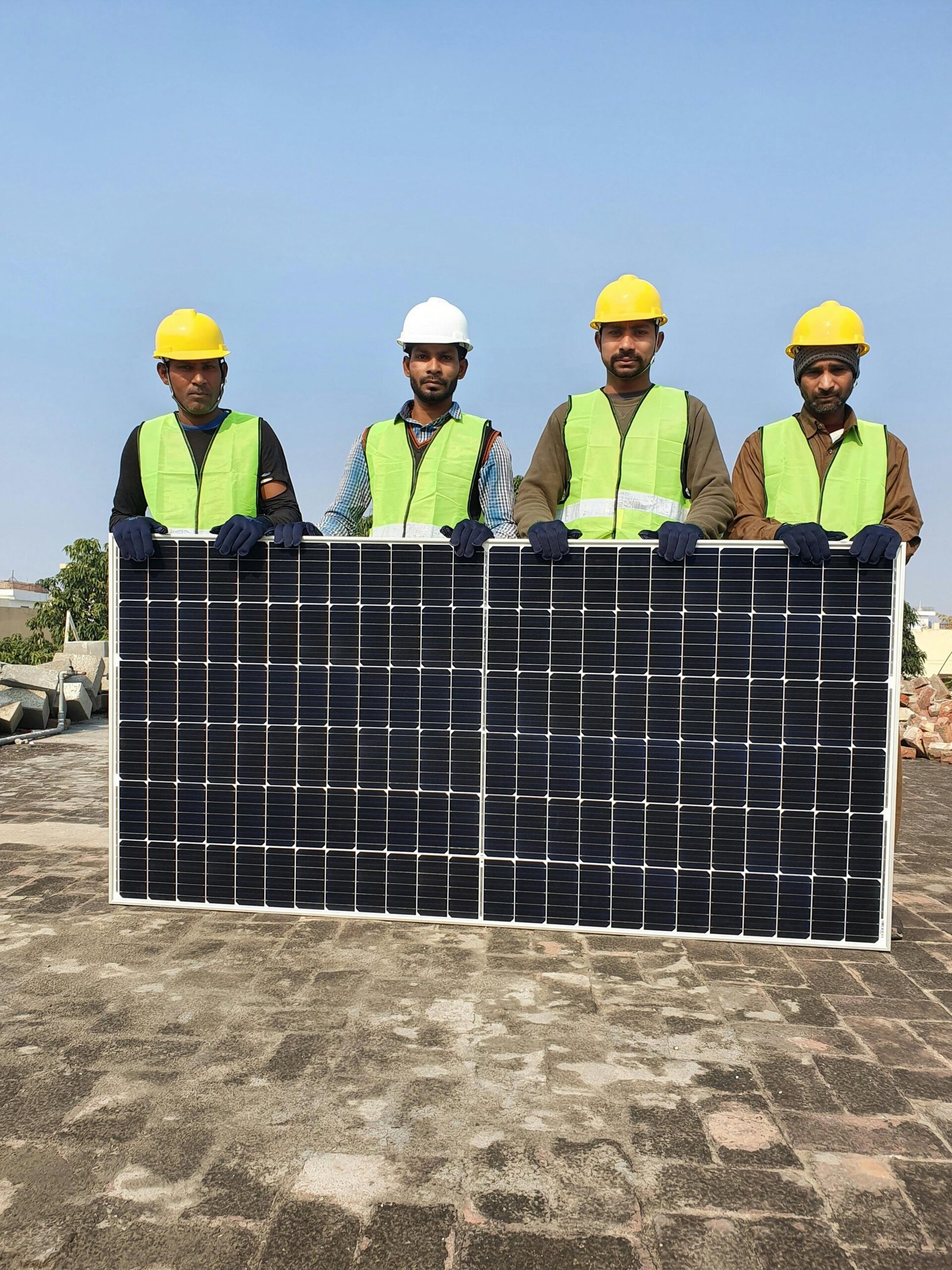 Four solar installation workers wearing hard hats and safety vests holding a large solar panel outdoors on a sunny day in Nevada